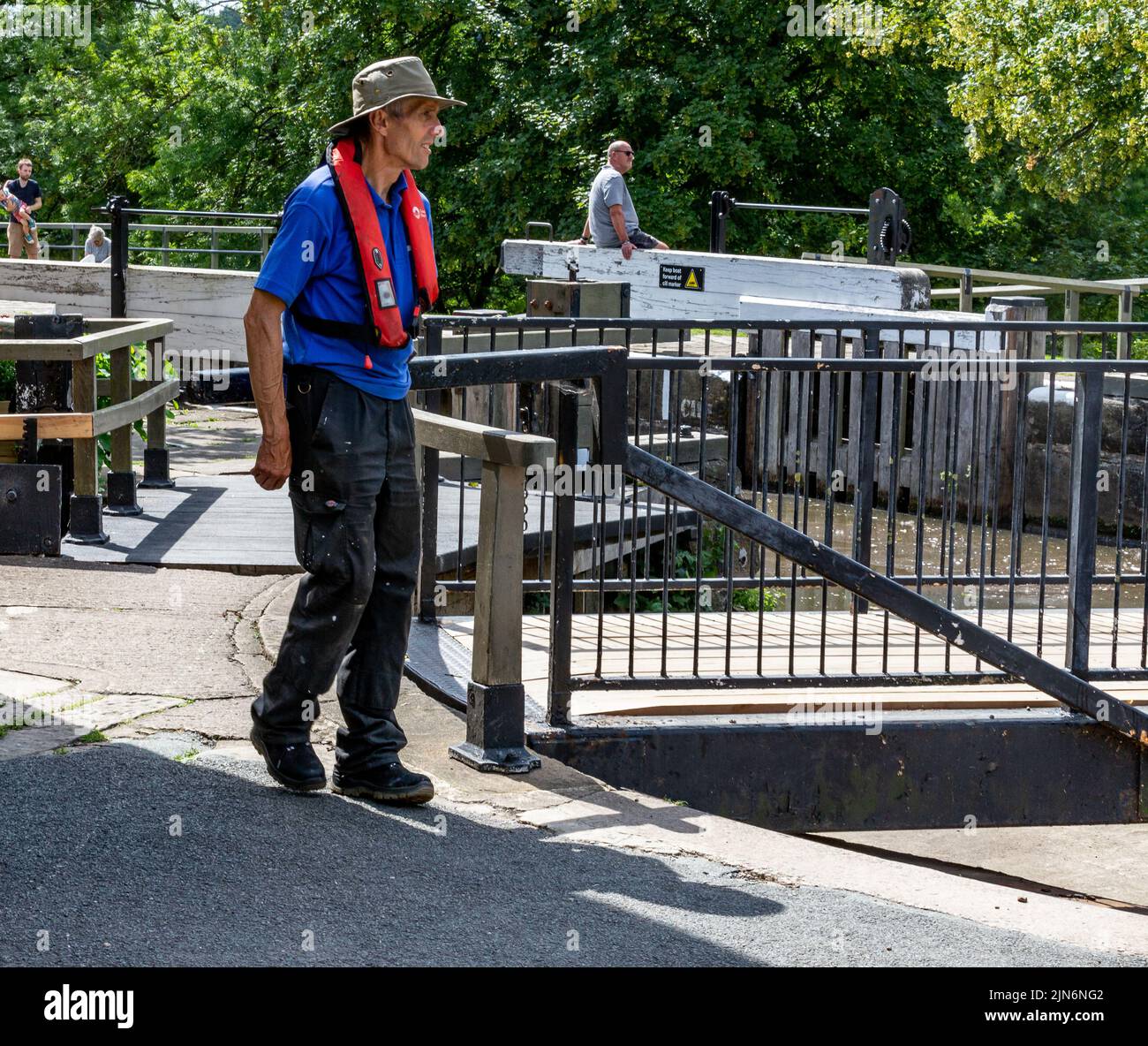 A Canal and River Trust lock keeper turning a swing bridge at the top of Five Rise Locks in Bingley, West Yorkshire. The top lock gates are opened. Stock Photo