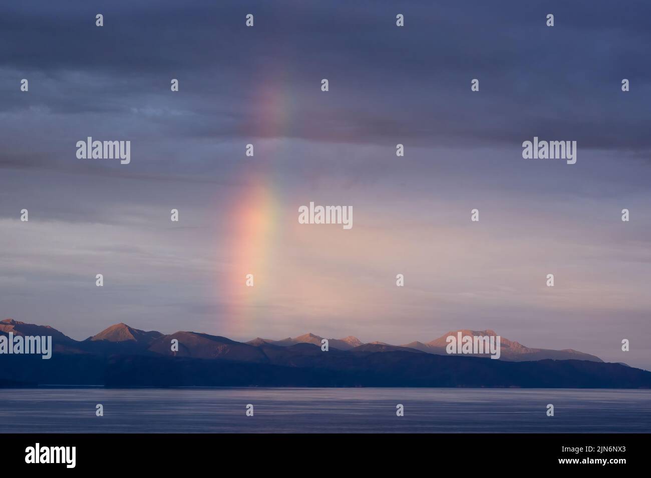 Rainbow at first light over Kenai Mountains across Kachemak Bay from Homer in Southcentral Alaska. Stock Photo