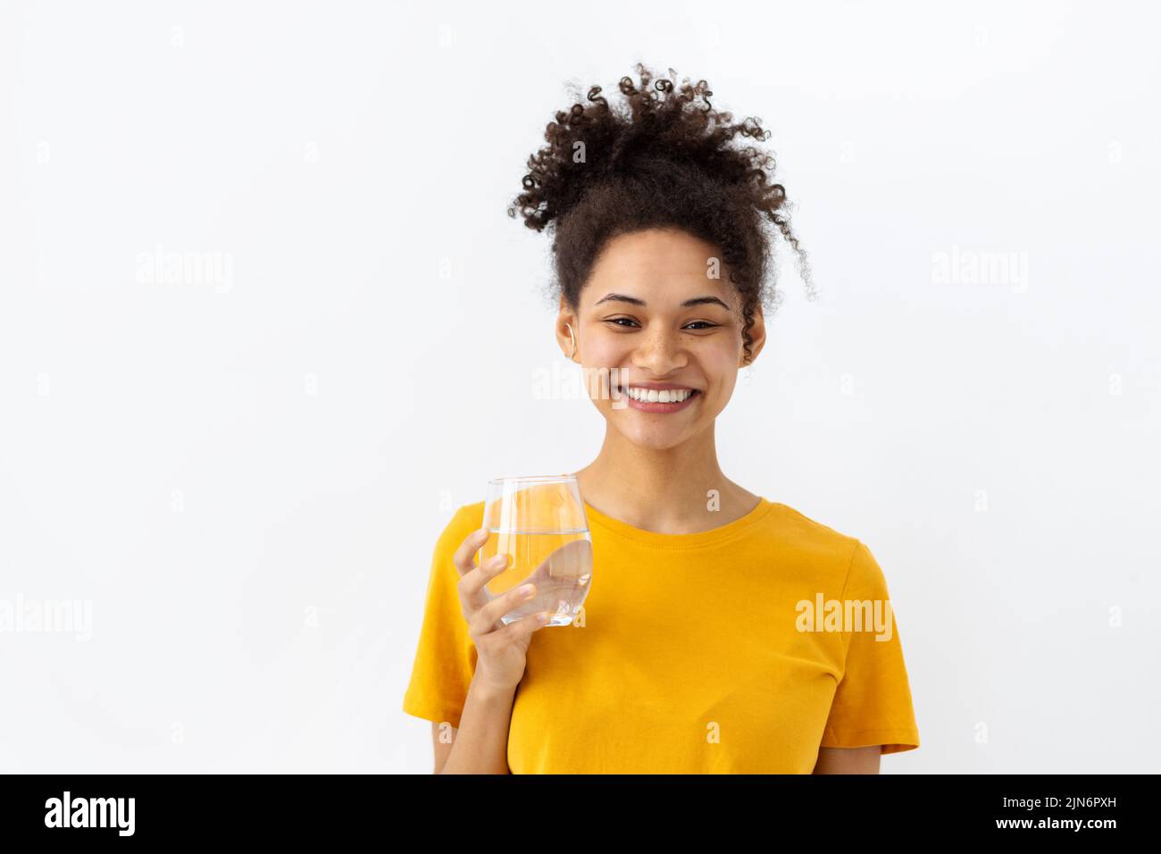 Smiling young woman holding glass of fresh clean water looking at ...