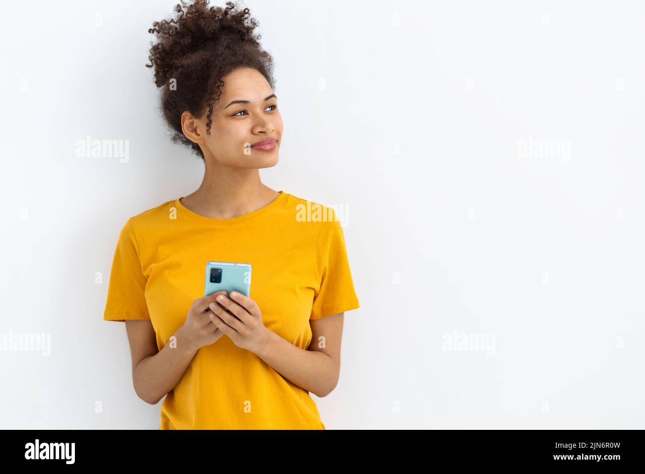 Beautiful young woman holding a mobile phone look away and about something dreaming smiling sweetly Stock Photo