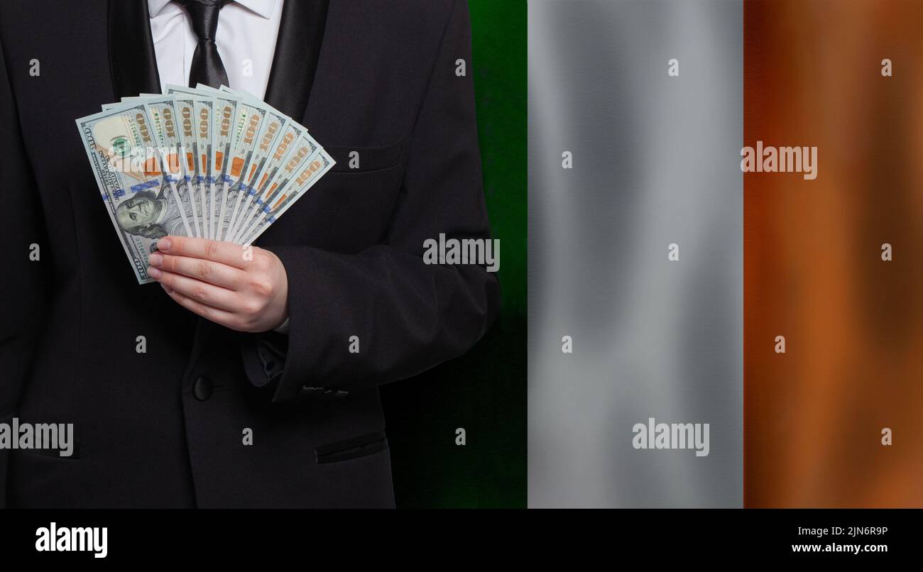Irish business man showing US 100 dollar bills against flag of Ireland