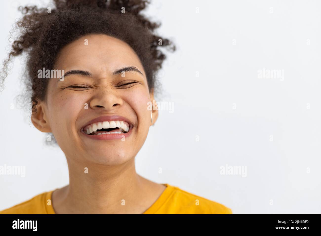 young happy positive woman with white teeth smiling broadly keeps eyes closed on white background Stock Photo