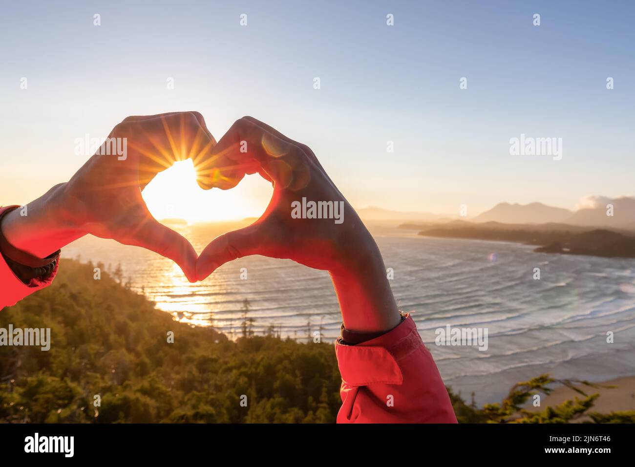 Adventurous Woman Hiker making heart shape with hands at Sandy Beach on the West Coast Stock Photo
