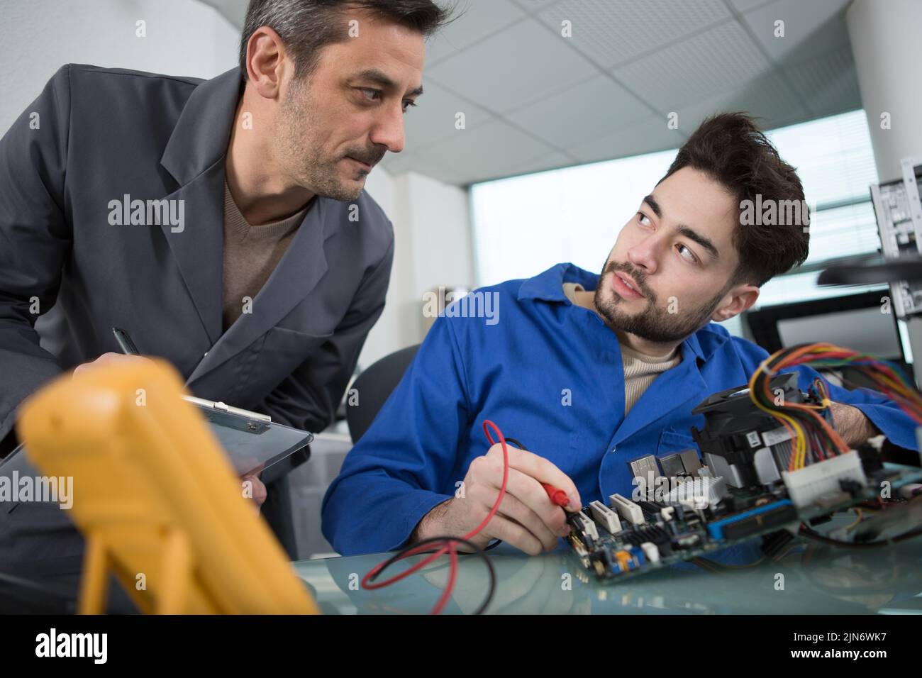 supervisor talking to electronics apprentice using multimeter Stock Photo