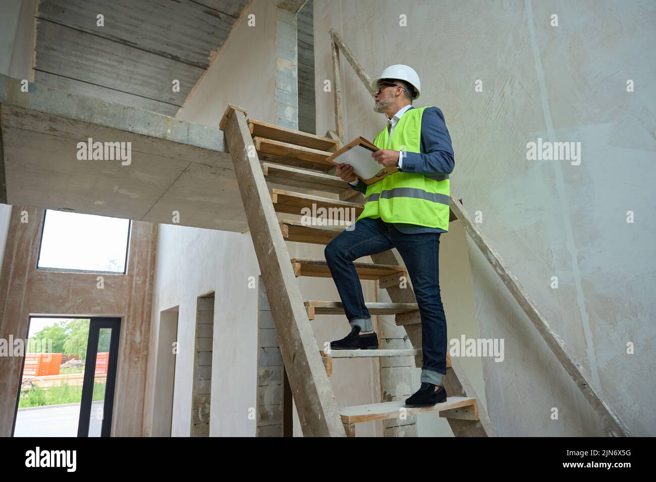 Male foreman climbs wooden ladder in unfinished house Stock Photo