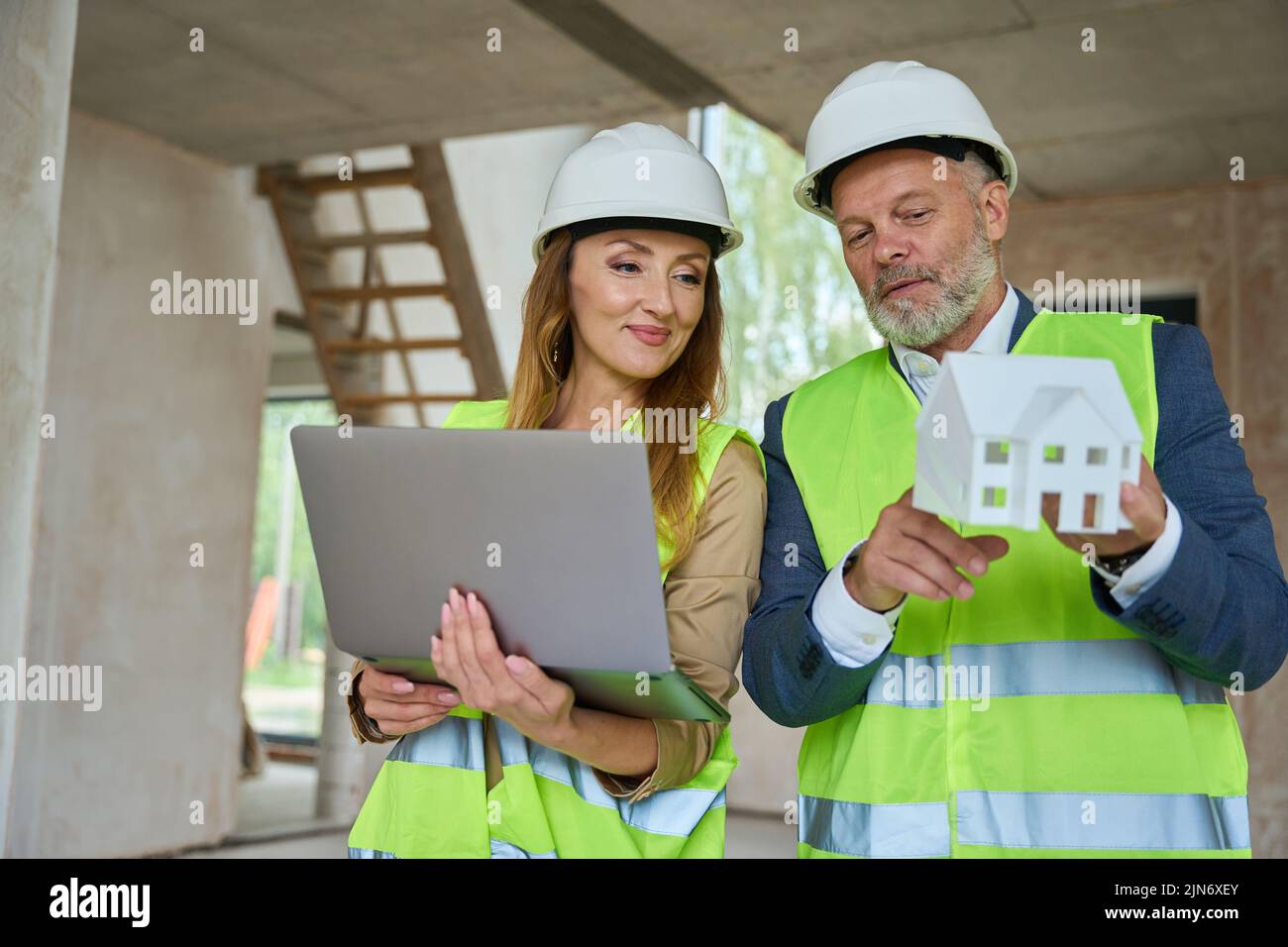 Realtor holds open laptop and looks at model house Stock Photo