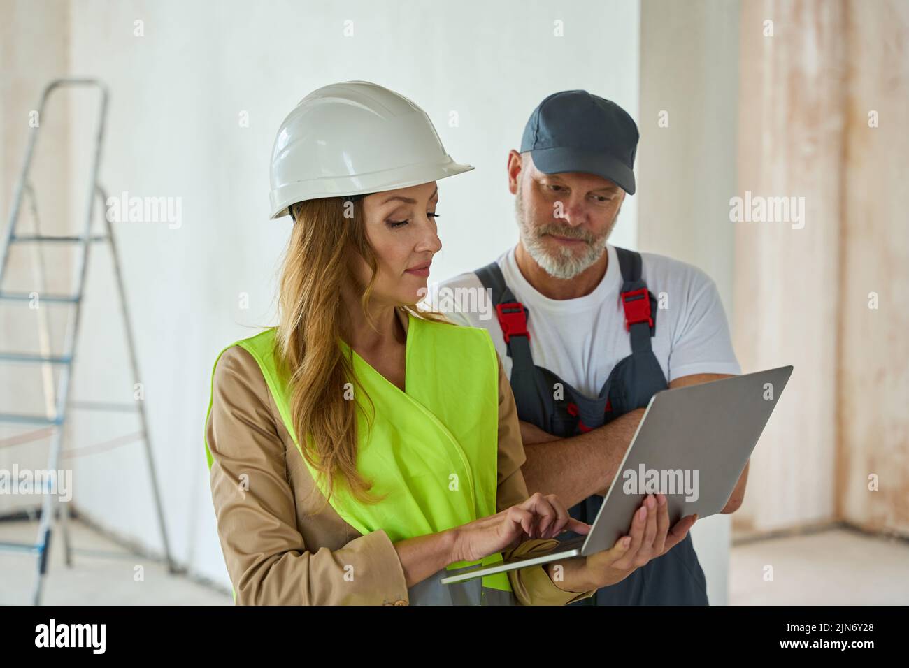 Manager holds open laptop and shows it to builder Stock Photo