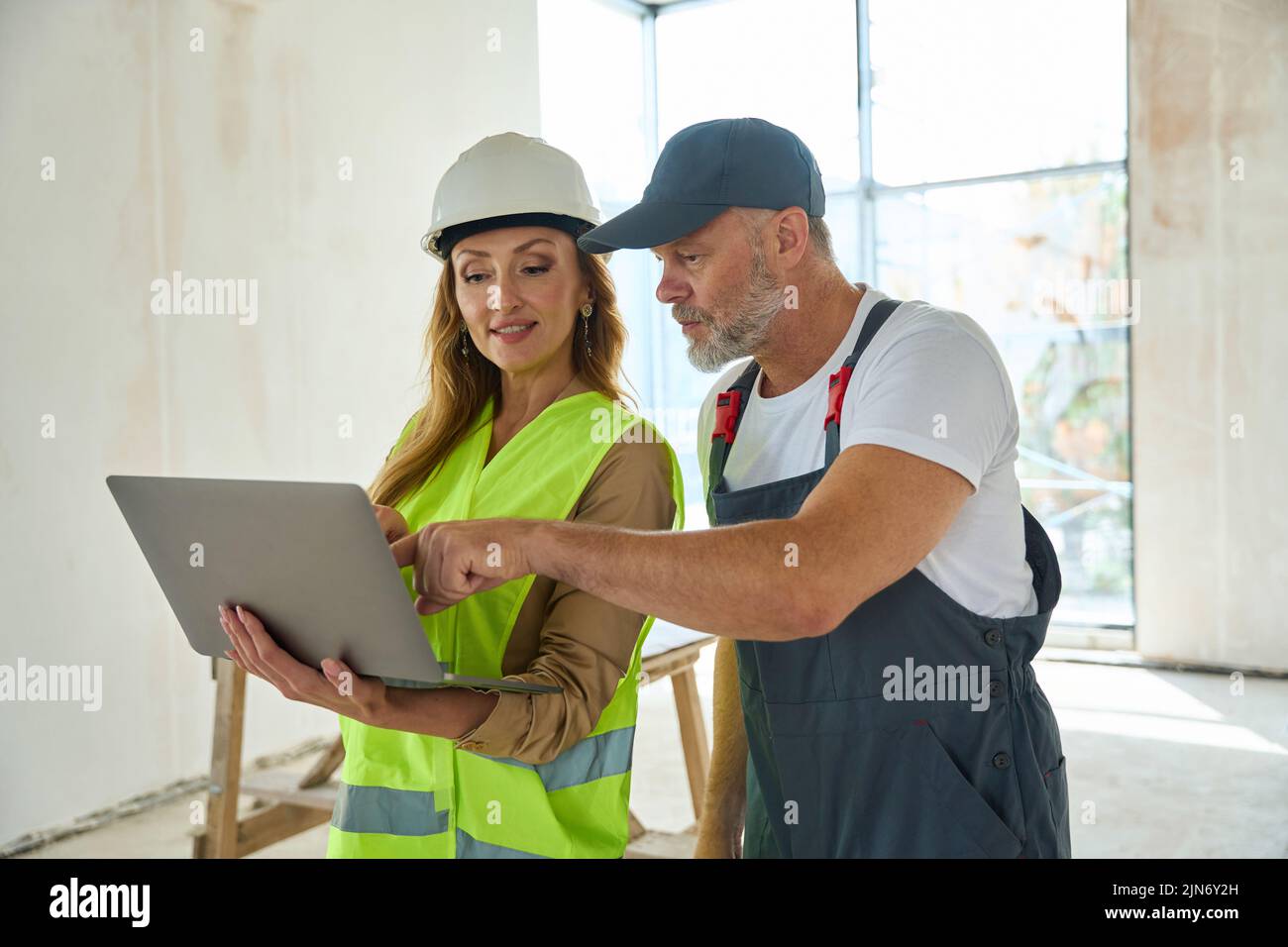 Gray-haired builder points finger at laptop held by sales manager Stock Photo