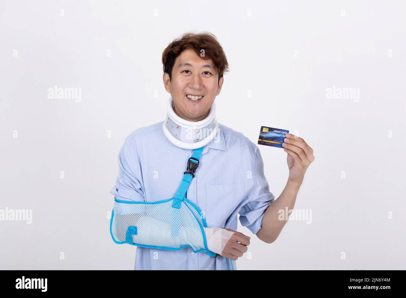 Portrait of a smiling handsome Asian man with broken arm and neck showing a credit card isolated on white background copy space Stock Photo