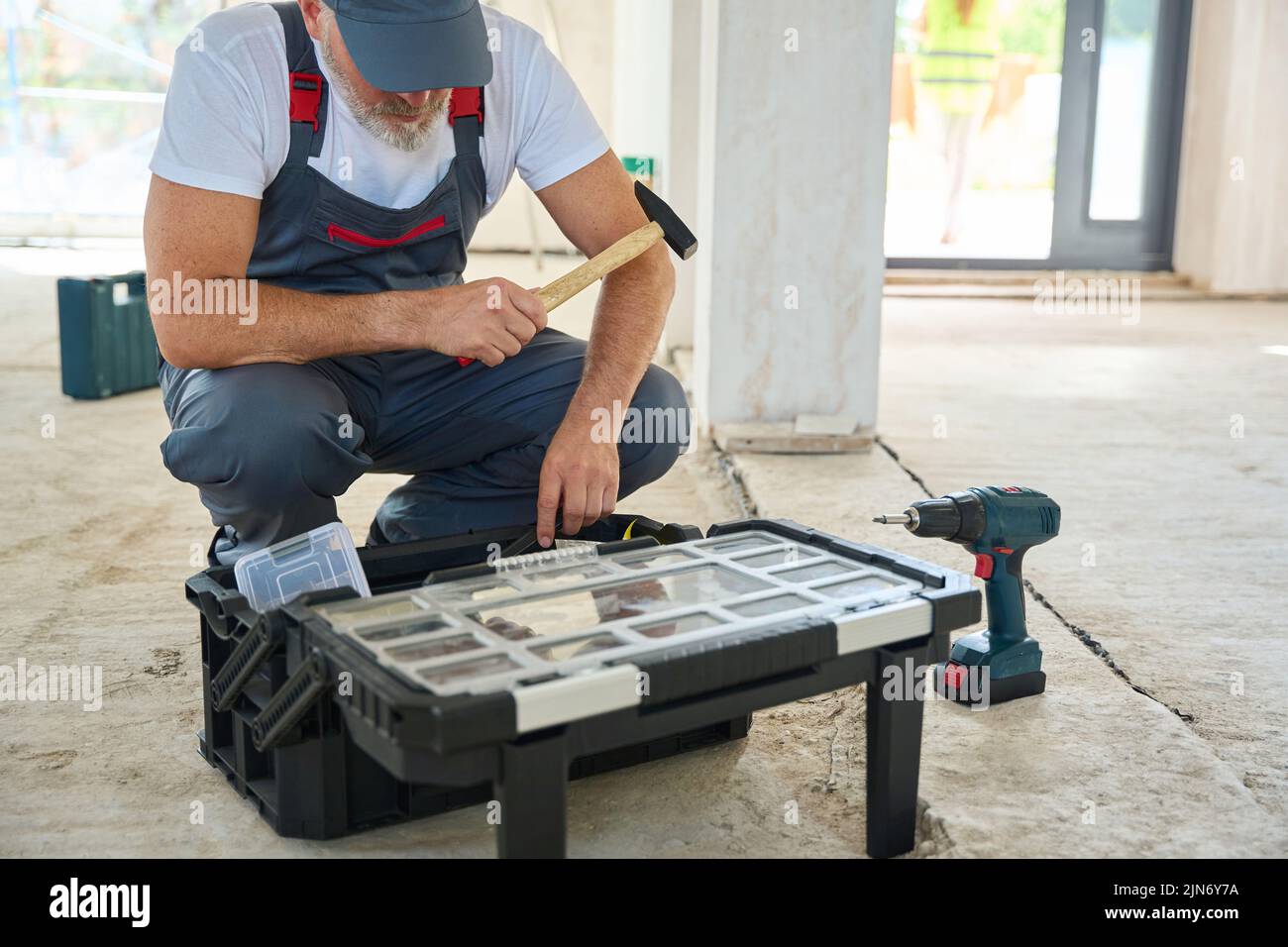 Bearded builder with hammer in his hand, looking into toolbox Stock Photo