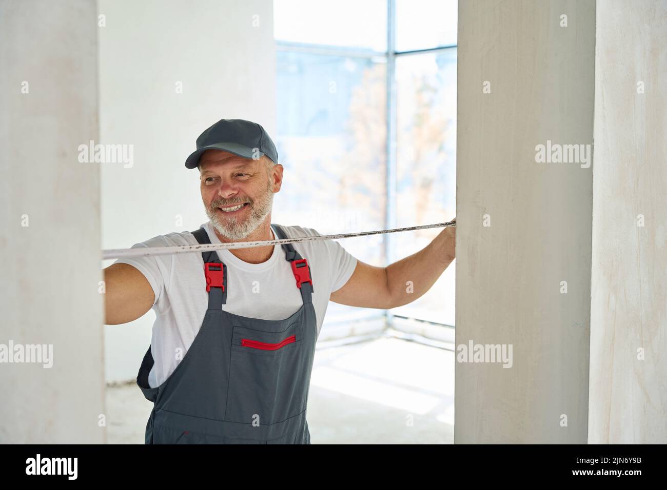 Joyful gray-haired builder measures width of doorway with tape measure Stock Photo