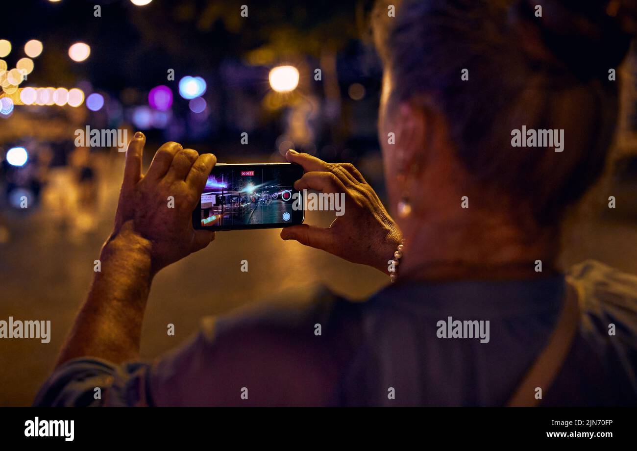 Adult mature elderly woman shutting a video of the evening city on a mobile phone Stock Photo