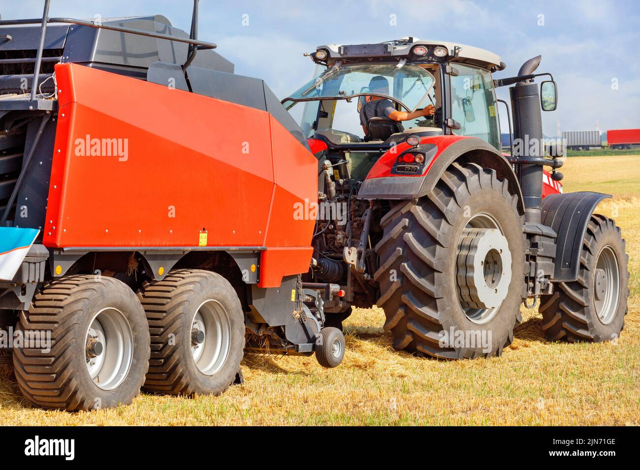 A tractor with a large red two-axle trailer for harvesting against the background of a harvested wheat field. Closeup. Stock Photo