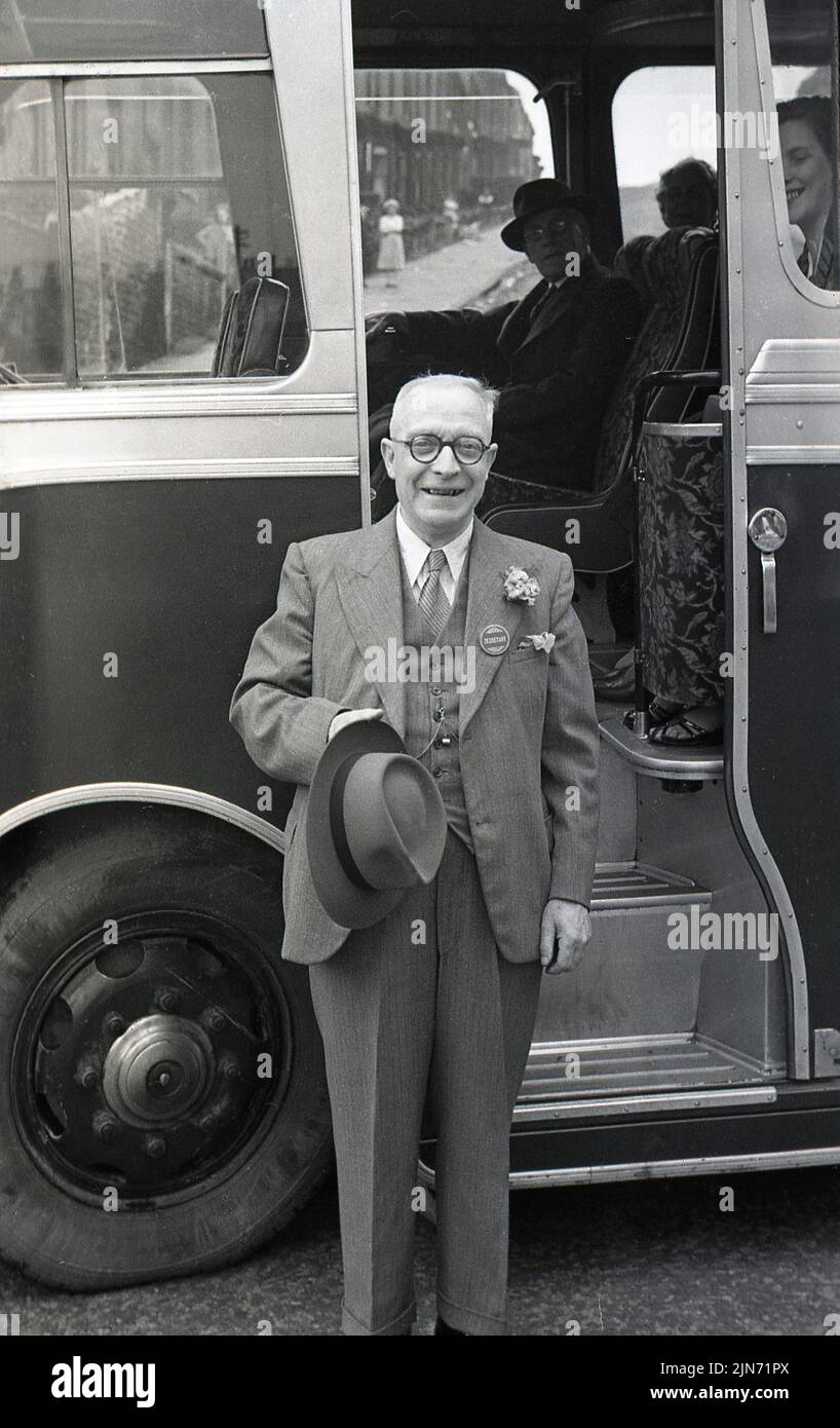 1950s, historical, coach trip, an elderly gentleman, dressed in suit & tie, flower in lapel and hat in hand, standing outside the entrance door to the coach, England, UK. On his suit lape, a badge with the word, Secretary. Stock Photo