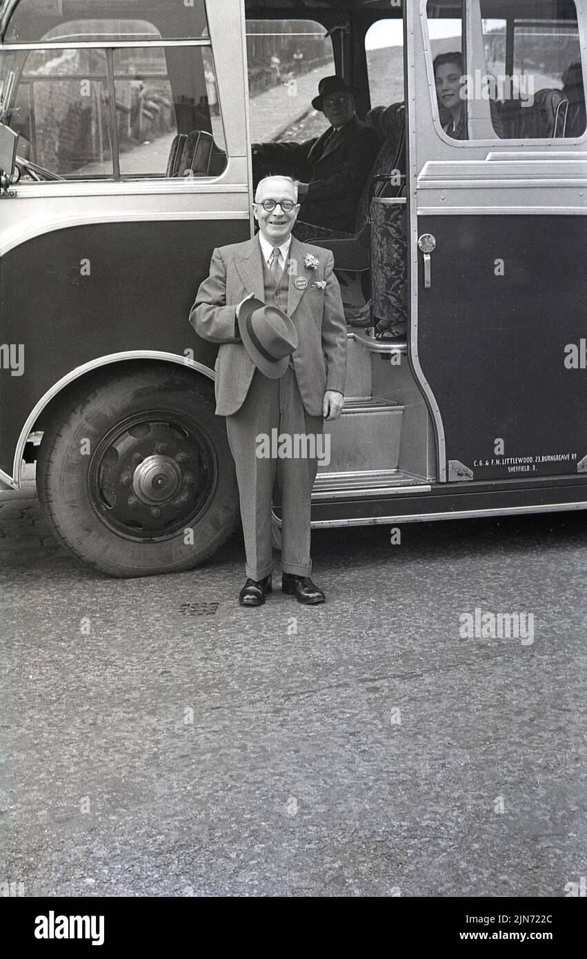 1950s, historical, coach trip, an elderly gentleman, dressed in a three-piece suit, jacket, waistcoat & tie, flower in lapel and hat in hand, standing outside the entrance door to the coach, England, UK. On his suit lape, a badge with the word, Secretary. Stock Photo
