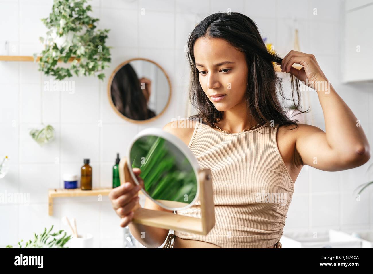 Young beautiful woman with dark skin looking into face mirror. Wellness, self-care concept Stock Photo