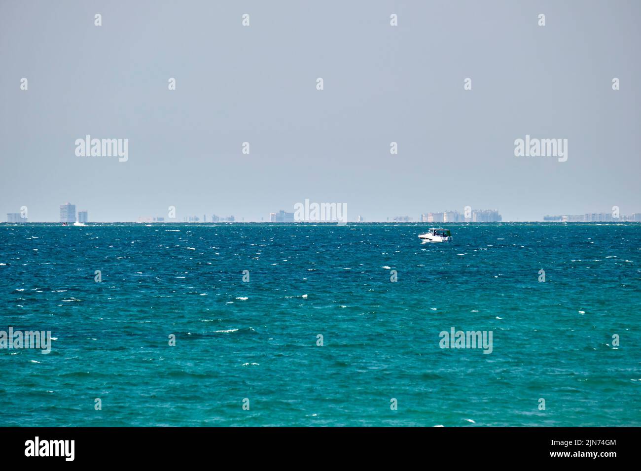 Sea panorama. Small motor boat floats in deap blue bay water under bright blue sky, tall buildings on distant shore Stock Photo