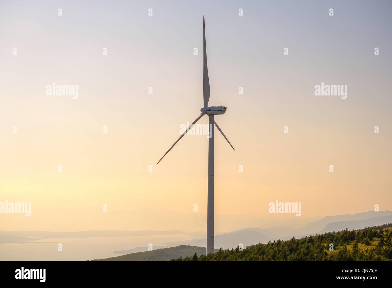 Wind turbine produces electrical green energy standing on coast of Adriatic Sea. Huge windmill converts wind power into electricity at sunset Stock Photo