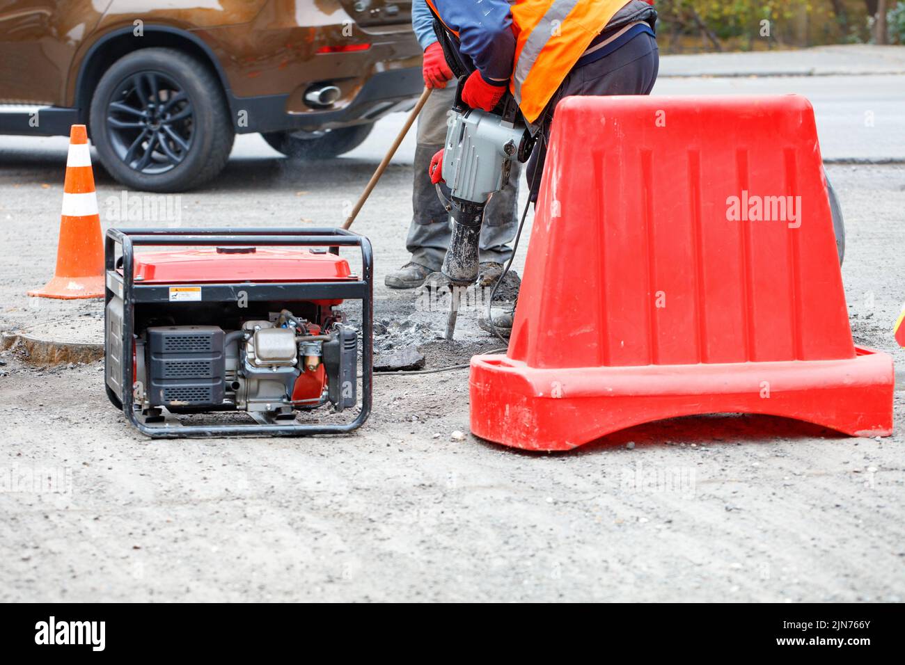 Road workers are repairing the carriageway of a section of the road with an electric jackhammer fenced with a red road shield. Stock Photo
