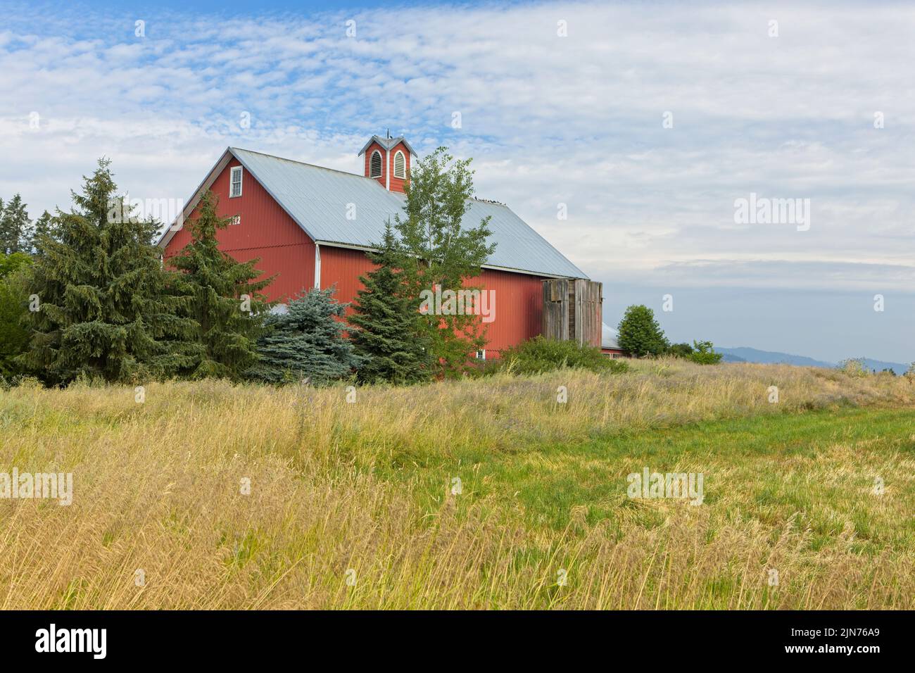 A bright red barn stands by a field in north Idaho. Stock Photo