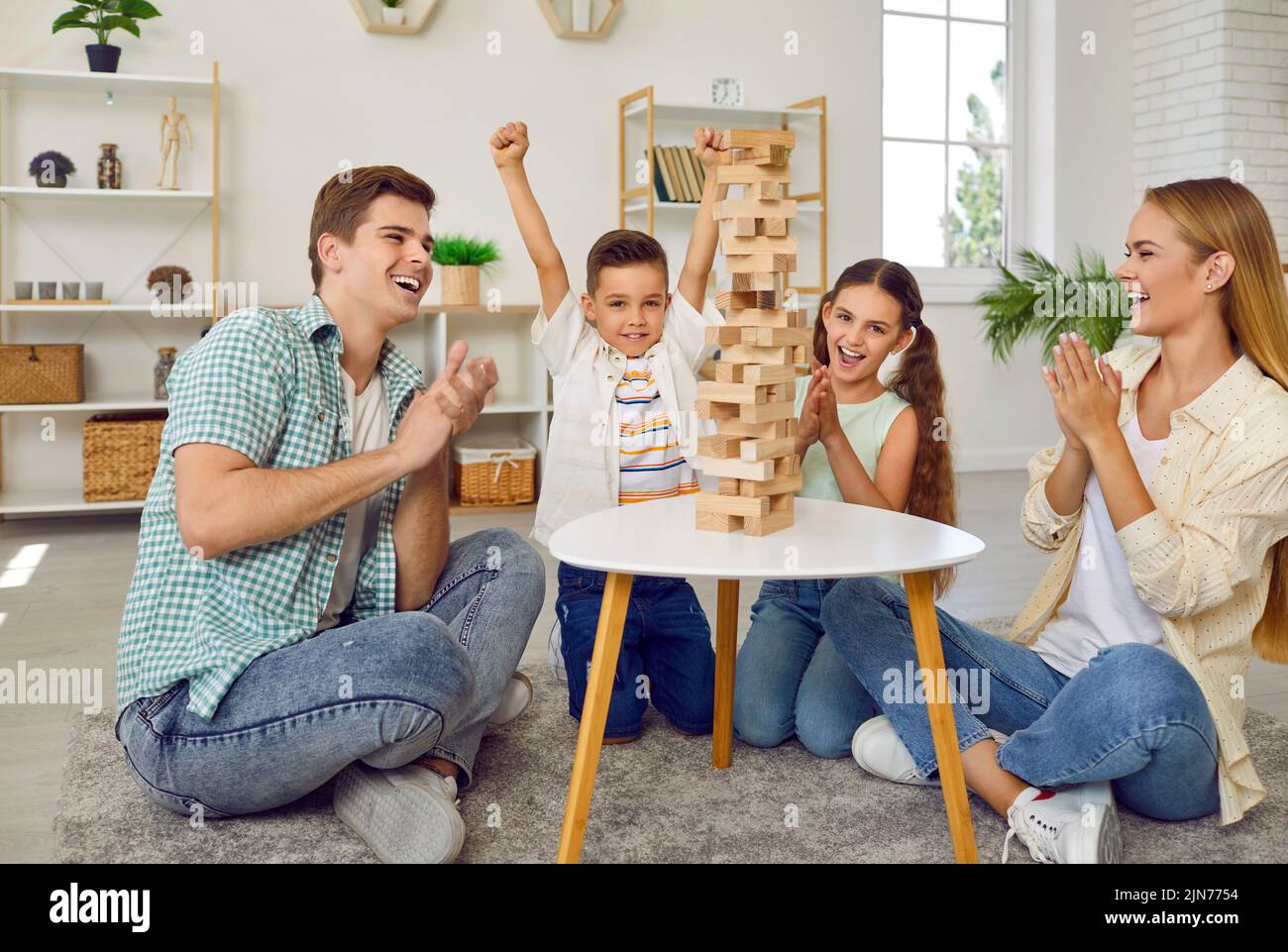 Cheerful and friendly young family with two children is having fun playing Jenga together. Stock Photo