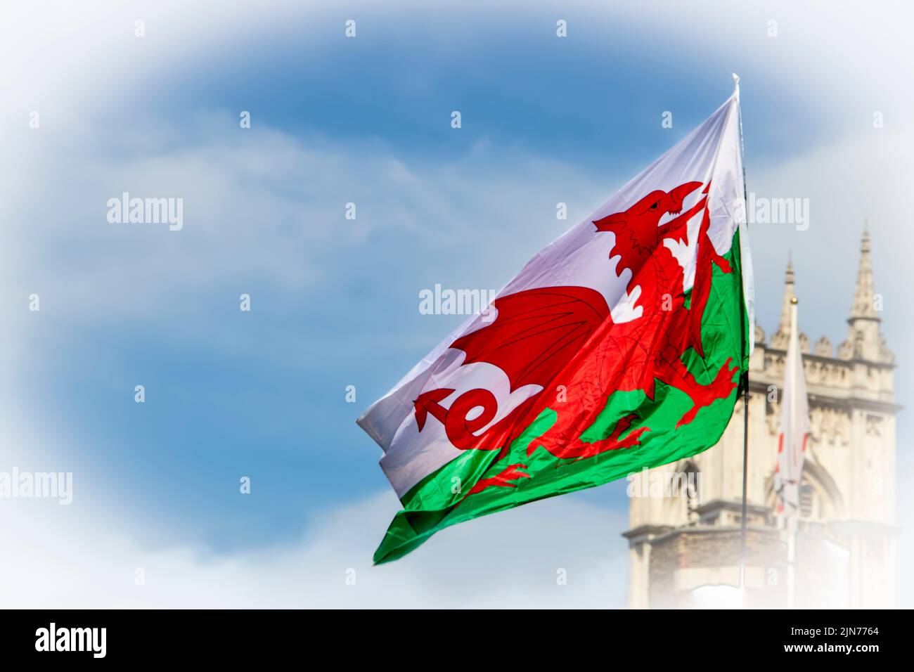 Welsh Dragon Flag flying in blue cloudy sky with the top of a castle like building in the background Stock Photo