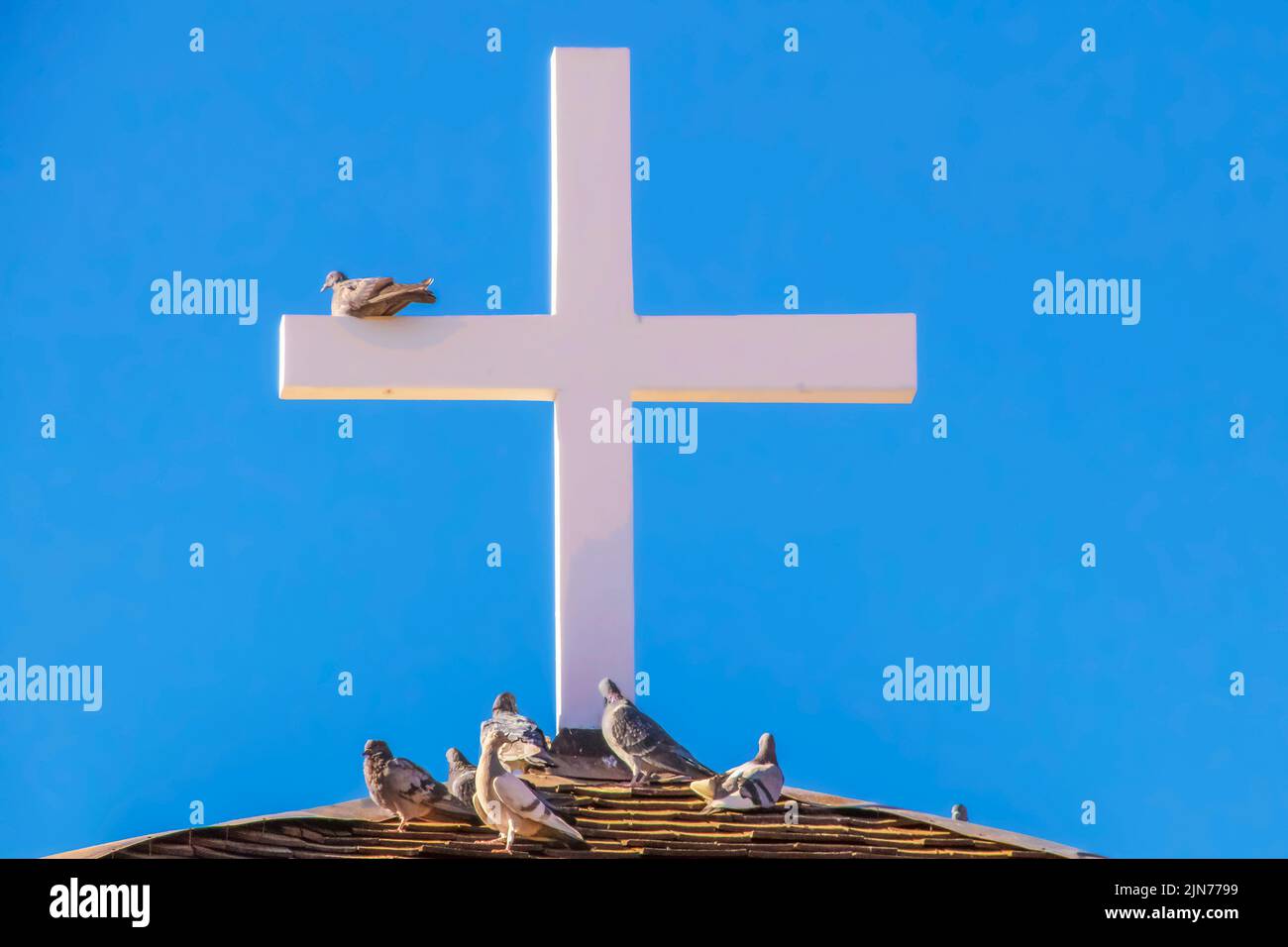 Wooden cross on roof against very blue sky with pigeons perching on it and below - close-up Stock Photo