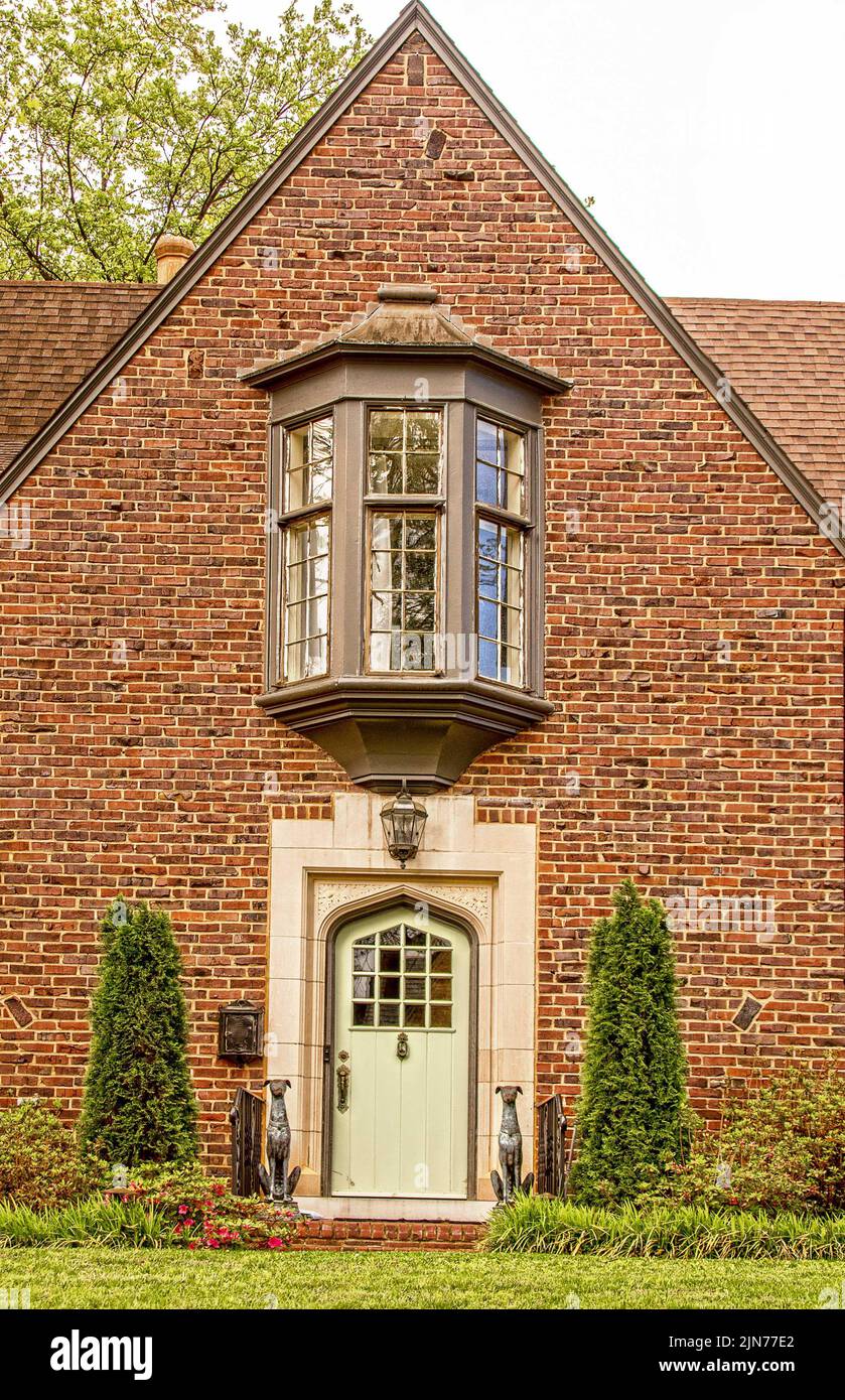 Brick house with bay window centered above the arched marble tiled door with statues of greyhoud dogs flanking the prorch - landscaping. Stock Photo