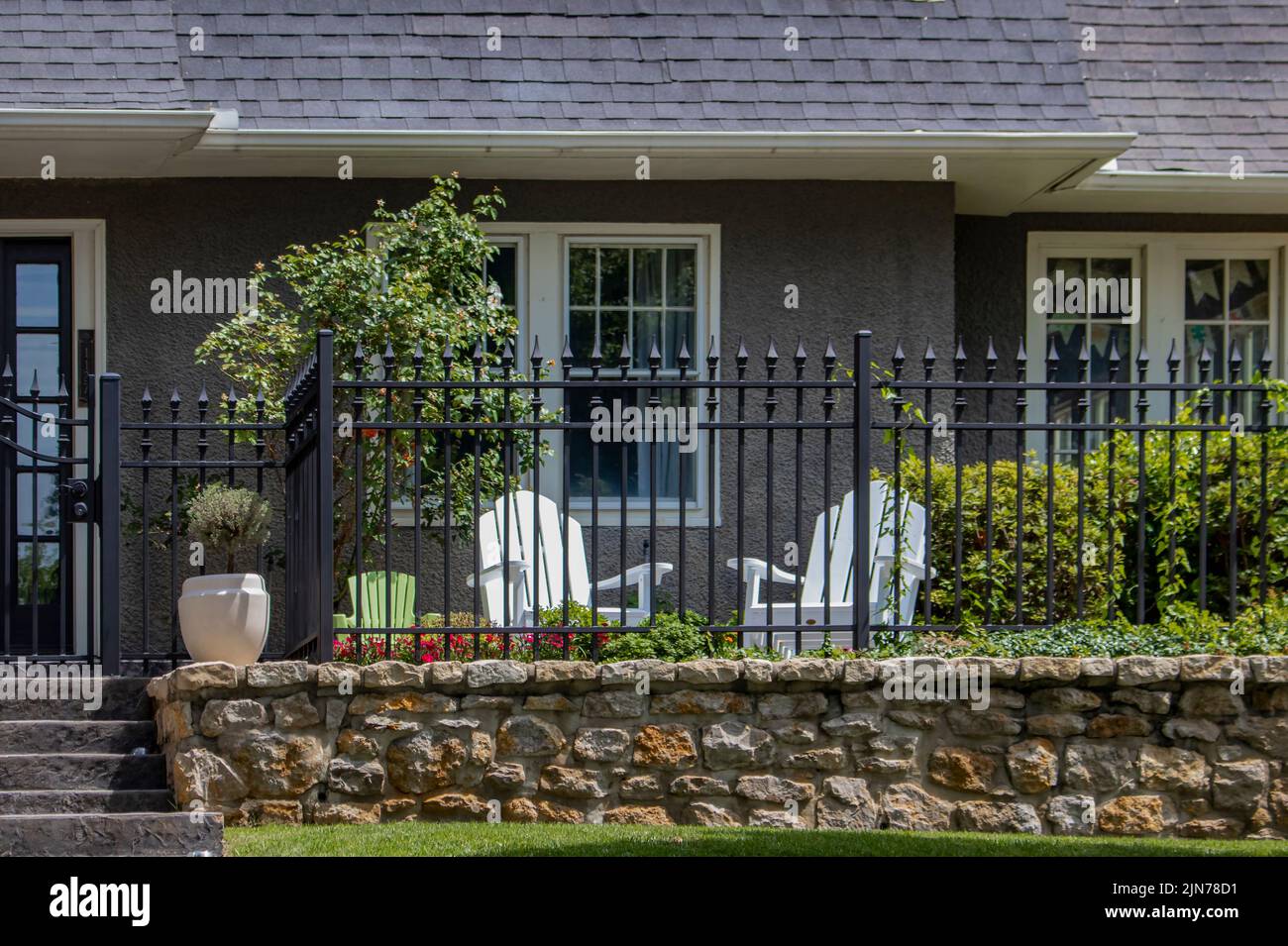 Small fenced garden area outside entrance to stucco house with two adult chairs and one childs chair Stock Photo