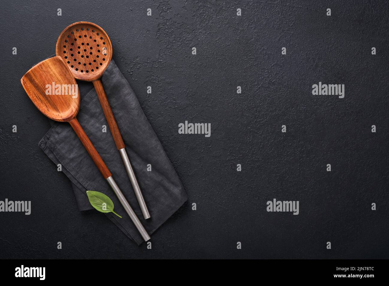 Cooking wooden utensils, basil leaves and spices on dark stone