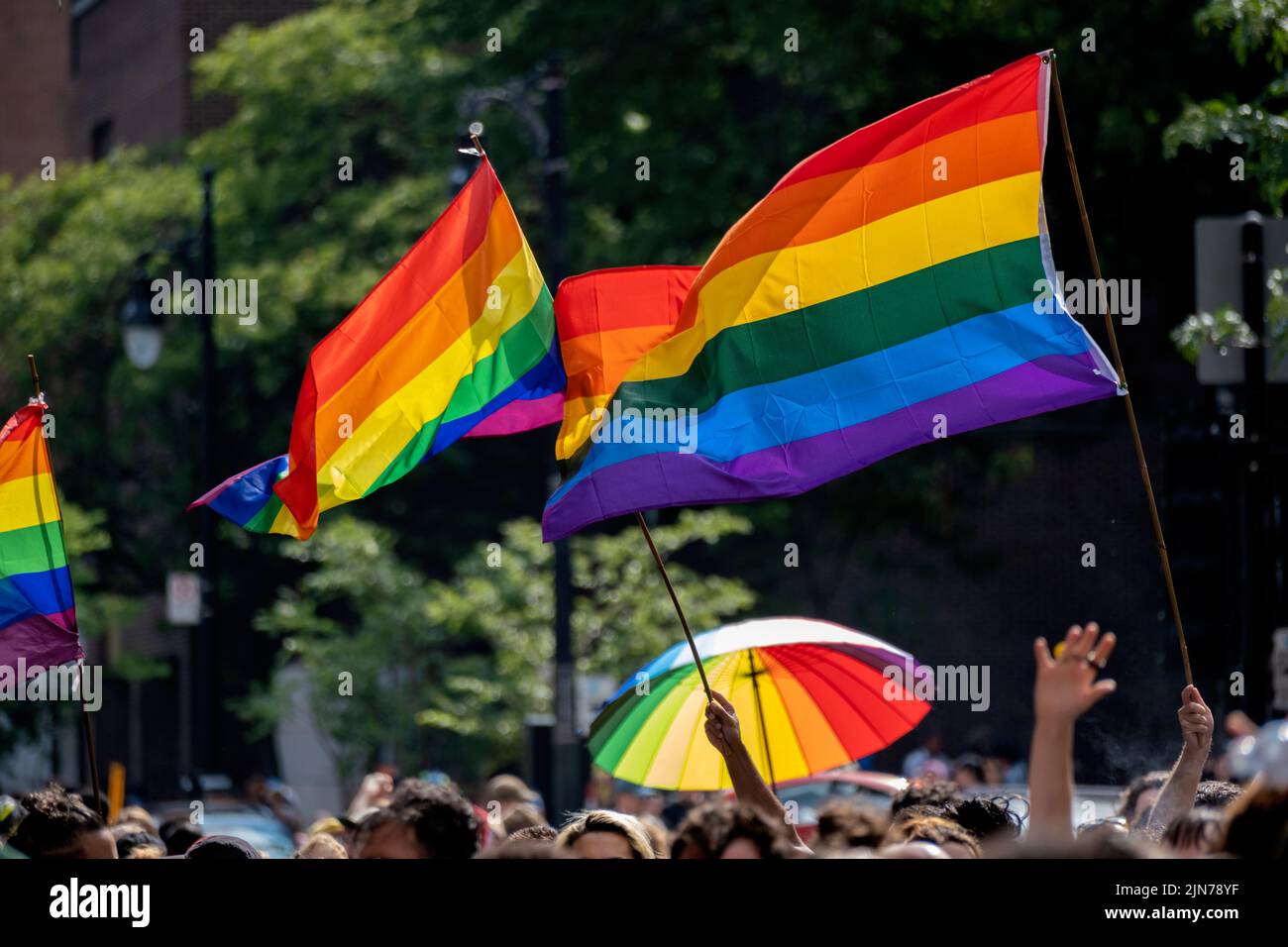 Montreal, CA - 7 August 2022: Gay rainbow flags waving above blurred crowd Stock Photo