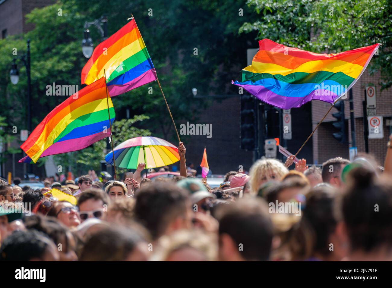 Montreal, CA - 7 August 2022: Gay rainbow flags waving above blurred crowd Stock Photo