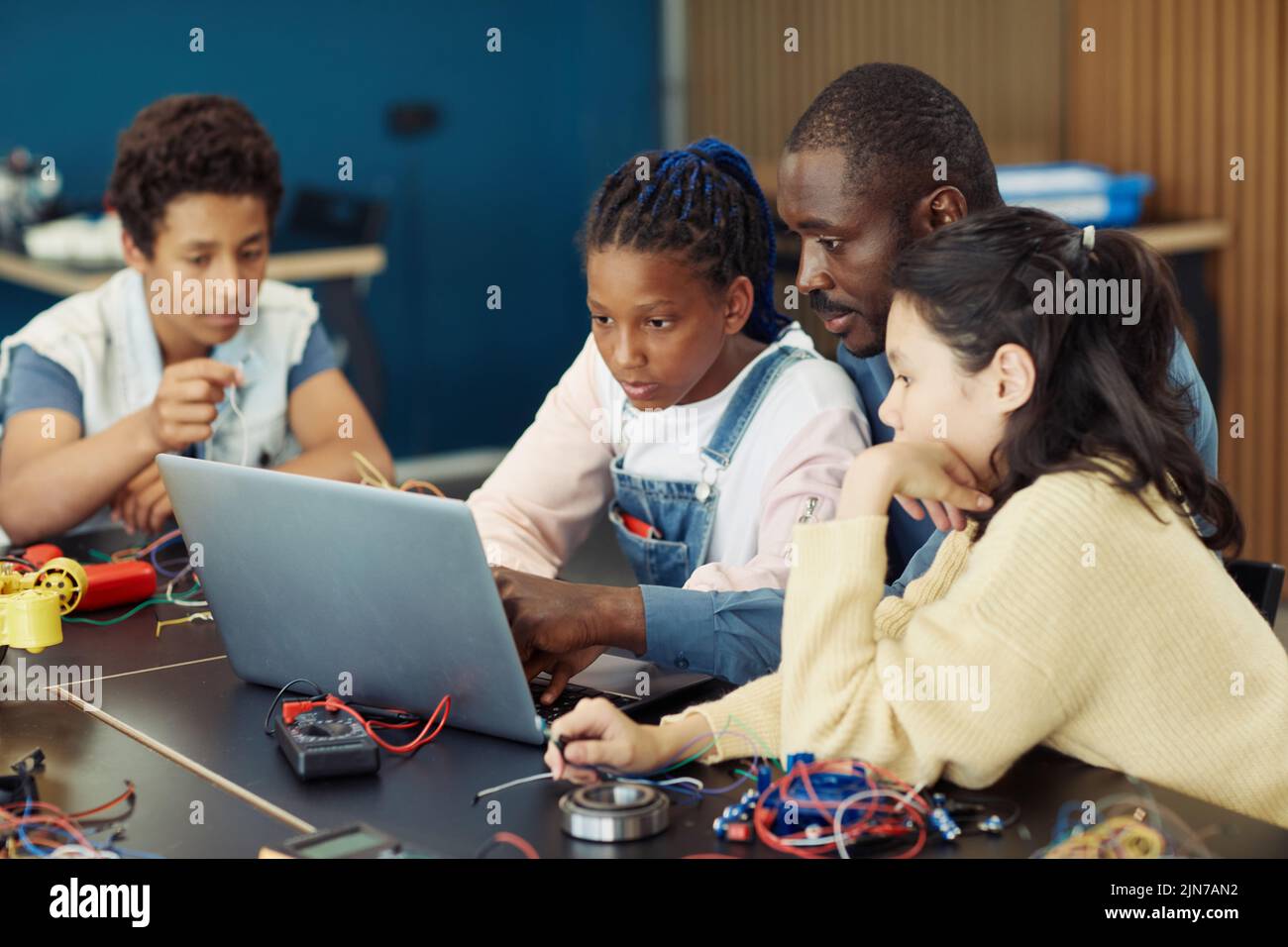 Portrait of black teenage girl using laptop in school during engineering class with male teacher and diverse group of children Stock Photo