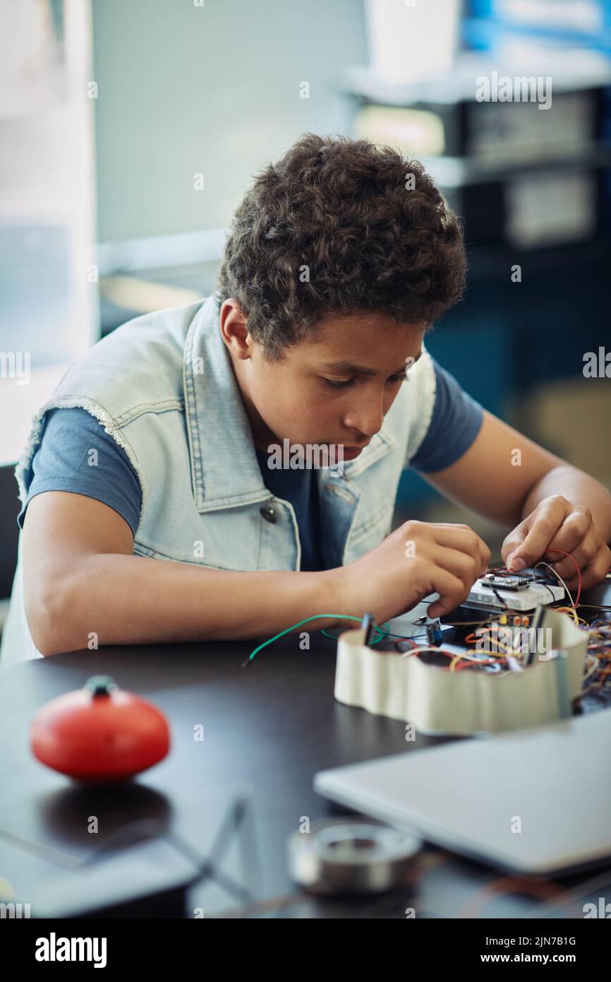 Vertical portrait of black teenage boy building robot and wiring circuit panel during engineering class at school Stock Photo