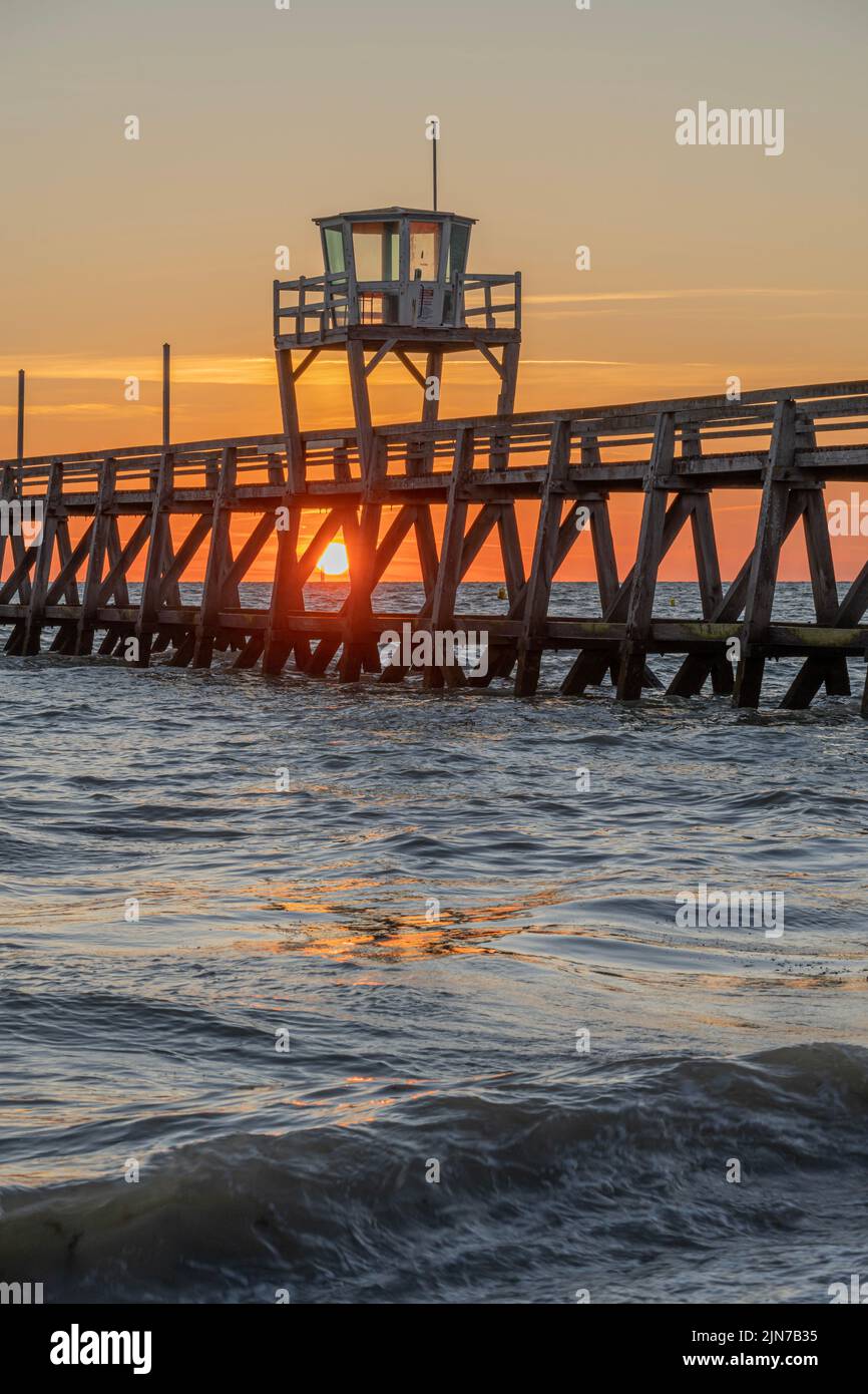 View of a wooden pier in front of the sea, a colorful sunrise and Le Havre city buildings far away Stock Photo