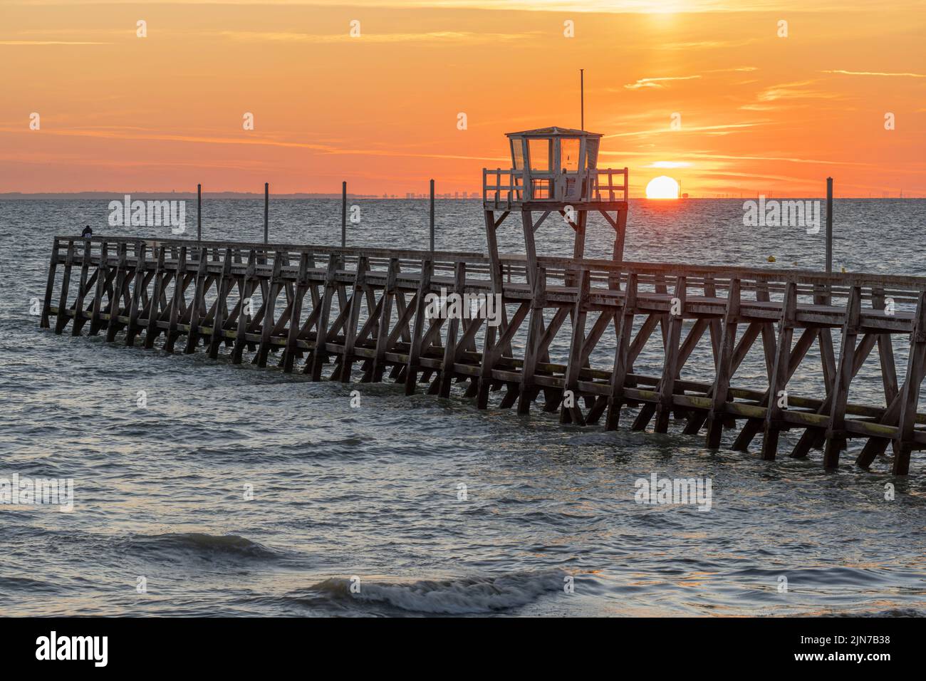 View of a wooden pier in front of the sea, a colorful sunrise and Le Havre city buildings far away Stock Photo