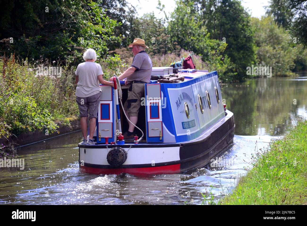 The Canal and River Trust has closed three stretches of popular waterway in Northern England due to low water levels. In early August 2022, the Trust took this step, meaning that other canals may be at risk of closure. Pictured is a narrow boat on the Bridgewater Canal in Cheshire, England, United Kingdom, with a man and a woman at the rear to control the boat's travel. Stock Photo