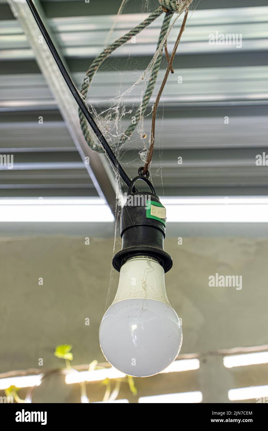 The energy saving light bulb hanging on a wire under the metal roof of a building Stock Photo