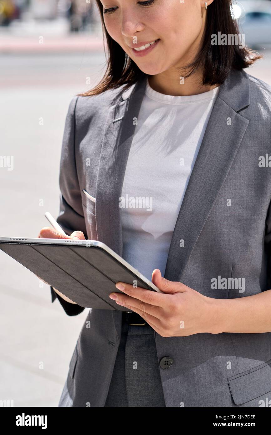 Young smiling Asian entrepreneur standing on city street using digital tablet. Stock Photo