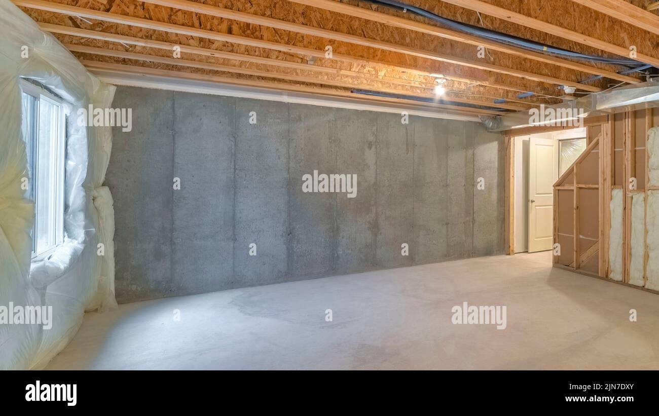 Panorama Unfinished basement with a plastic vapor barrier on the wall. Empty basement interior