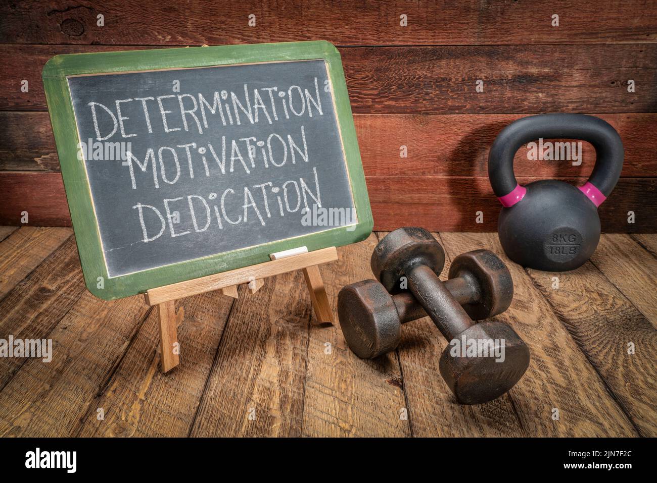 determination, motivation and dedication - inspirational text in white chalk on a slate blackboard with dumbbells and kettlebell, fitness concept Stock Photo