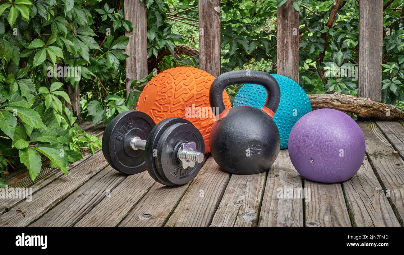 three heavy slam balls, iron kettlebell and dumbbell on a backyard deck, home and backyard gym concept Stock Photo