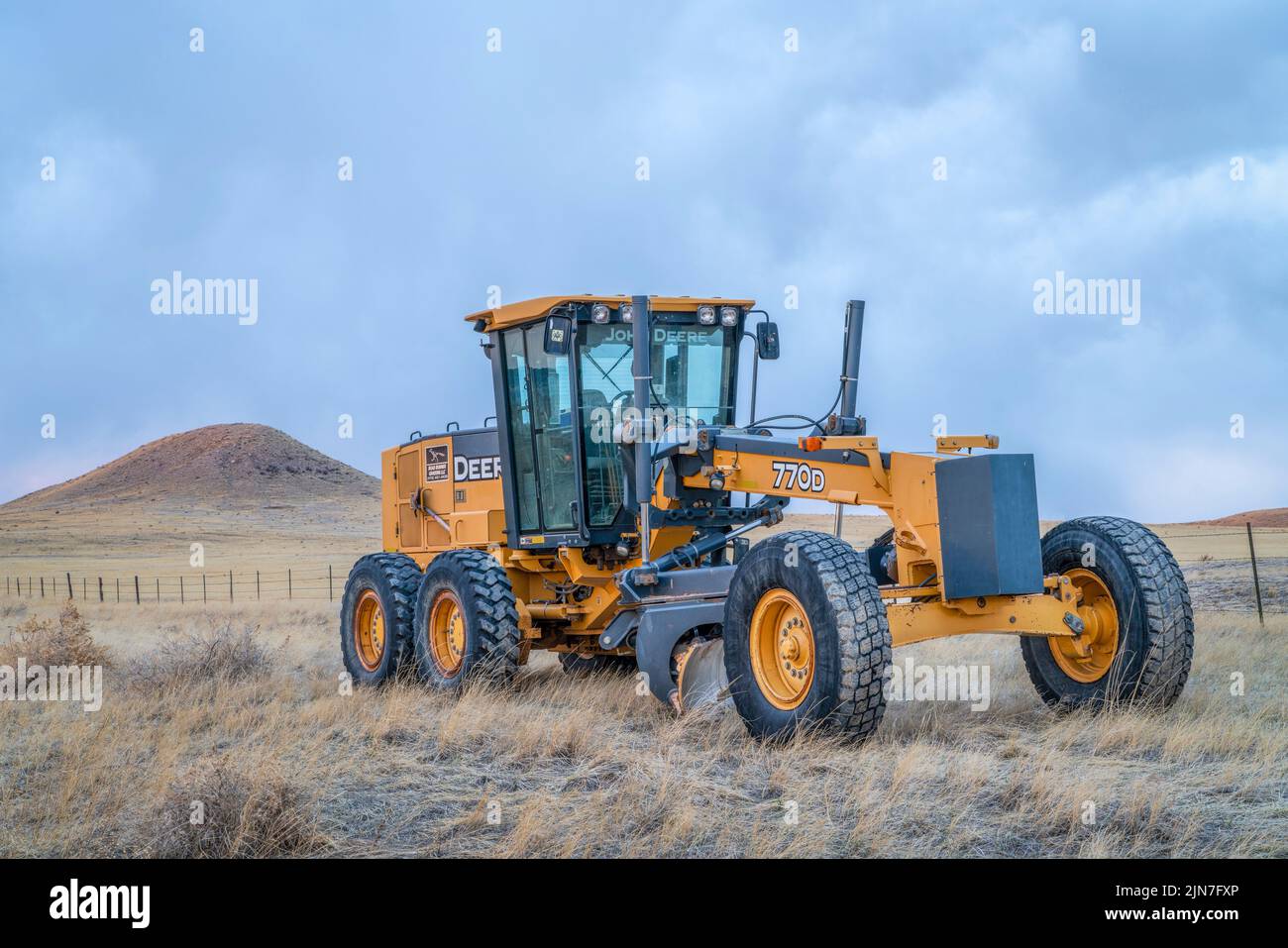 Fort Collins, CO, USA - March 31, 2022: Deere 770D motor grader at Colorado foothills used for dirt road maintenance, early spring scenery at dusk. Stock Photo