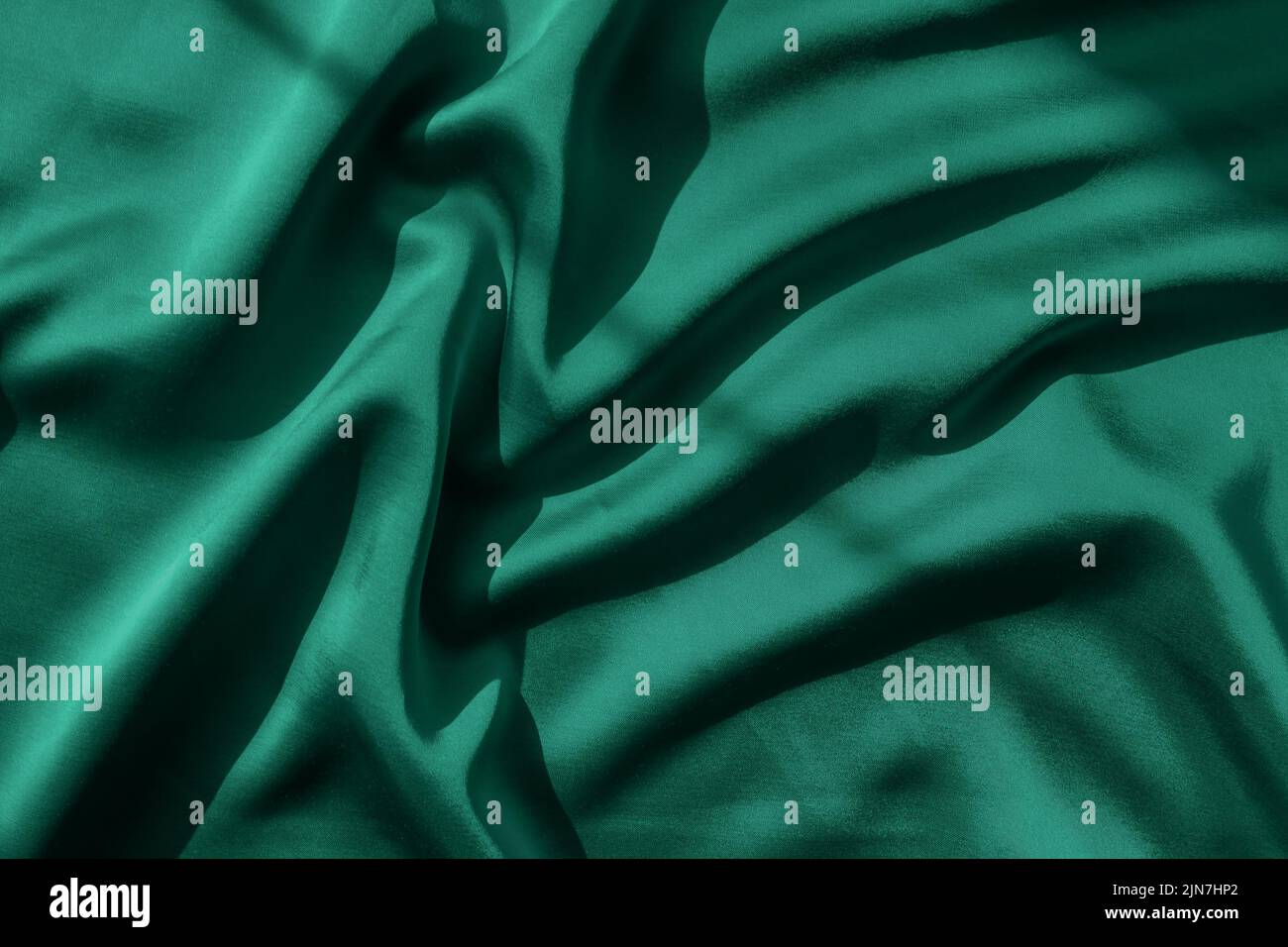 Emerald green tone satin fabric with folds in natural sunlight Stock