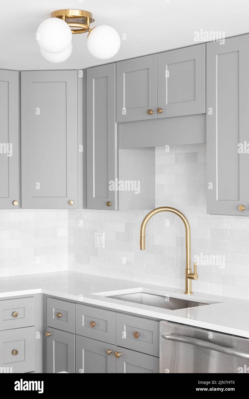 A kitchen sink detail shot with a gold faucet, marble backsplash, grey
