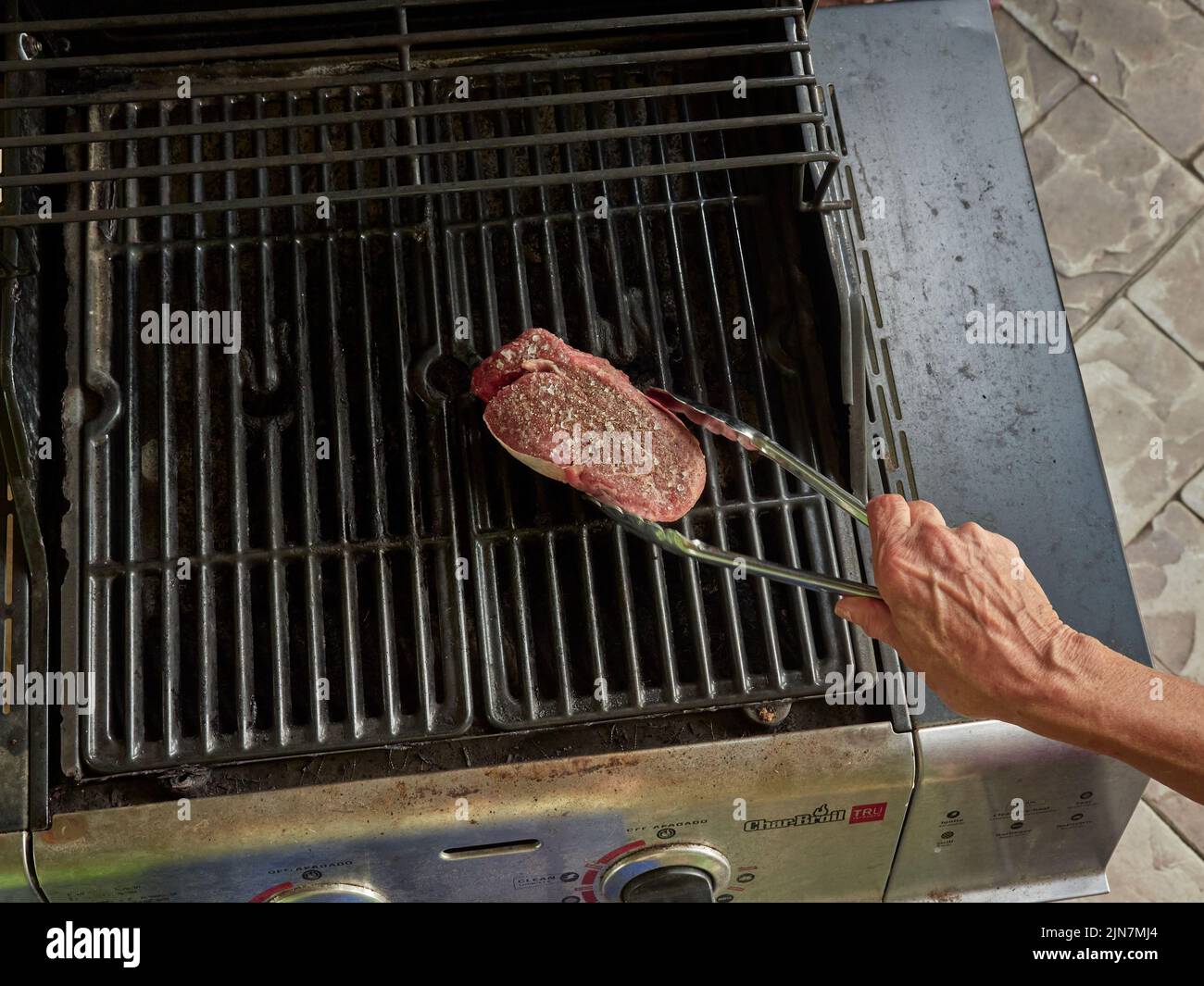 Person placing a raw filet steak on a barbecue grill to cook the red meat for dinner. Stock Photo