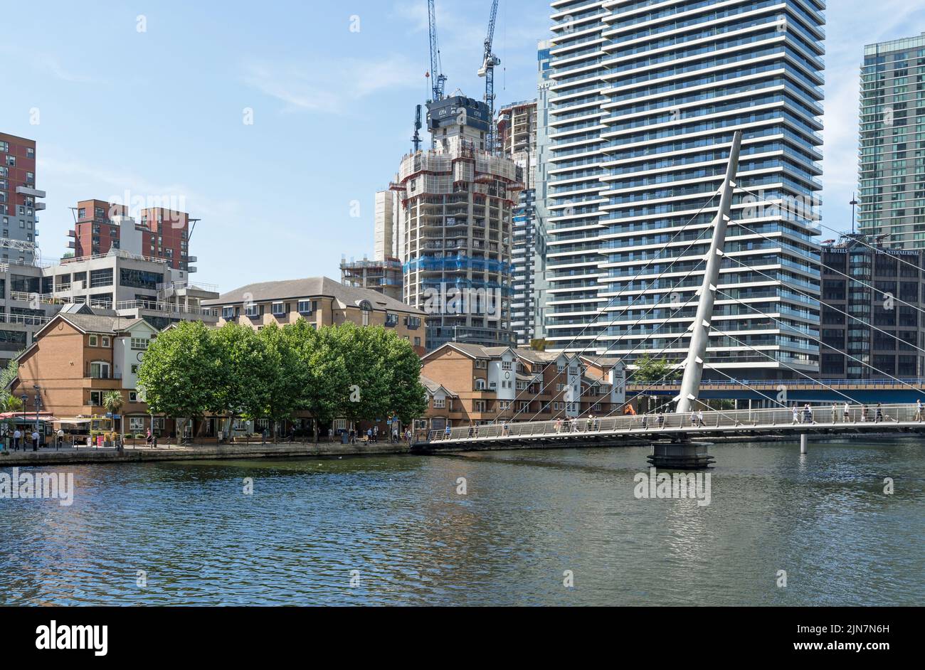 The South Quay Footbridge on a sunny day in Canary Wharf with construction work of new apartment buildings in the distance. London - 9th August 2022 Stock Photo
