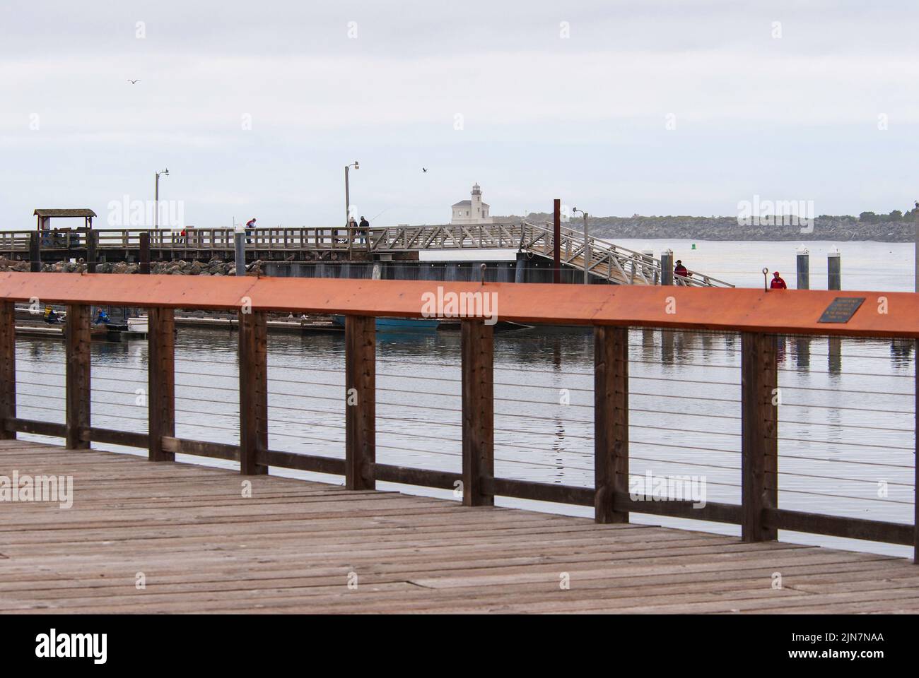 A boardwalk looks out upon a fishing pier in the Pacific Northwest with Coquille River lighthouse in the distance on a foggy day. Near Bandon, Oregon, Stock Photo