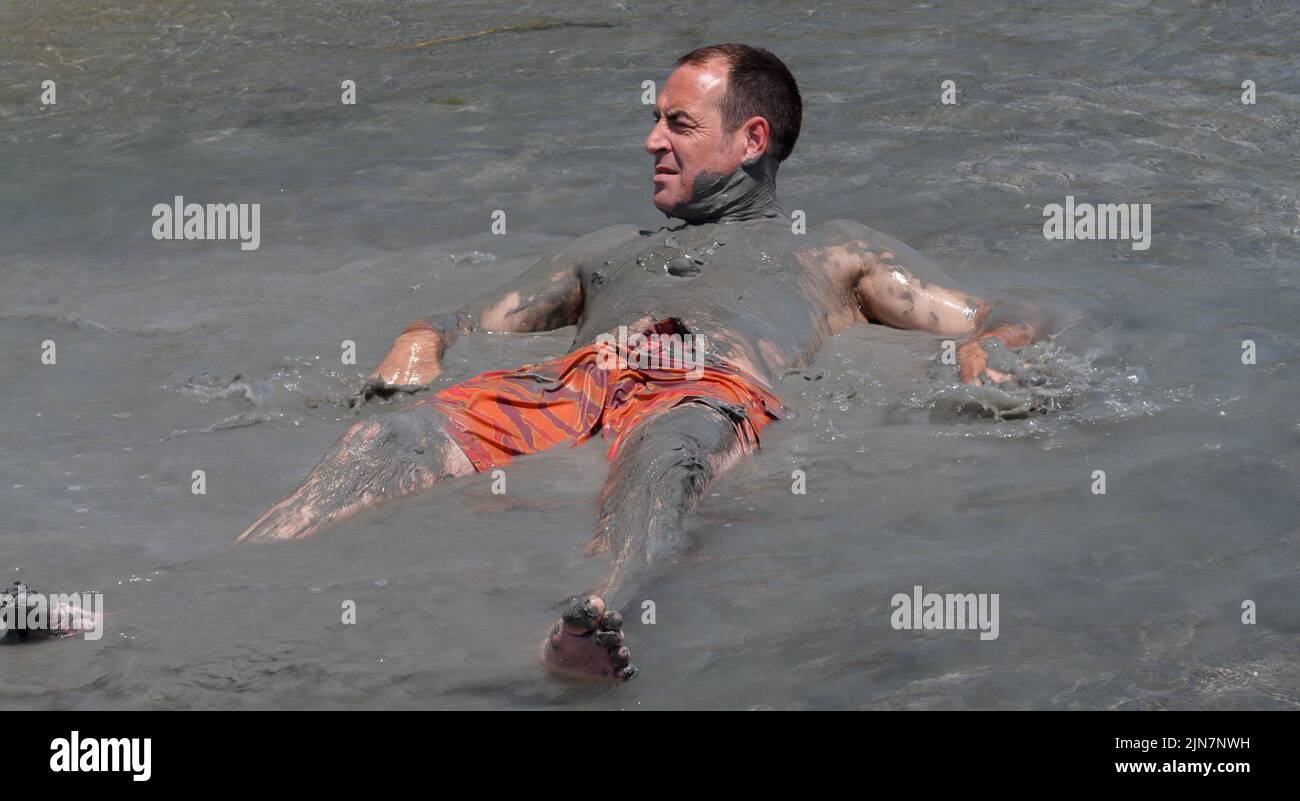 Mud Bath. A man lays in a mud pool and covers himself with mineral rich