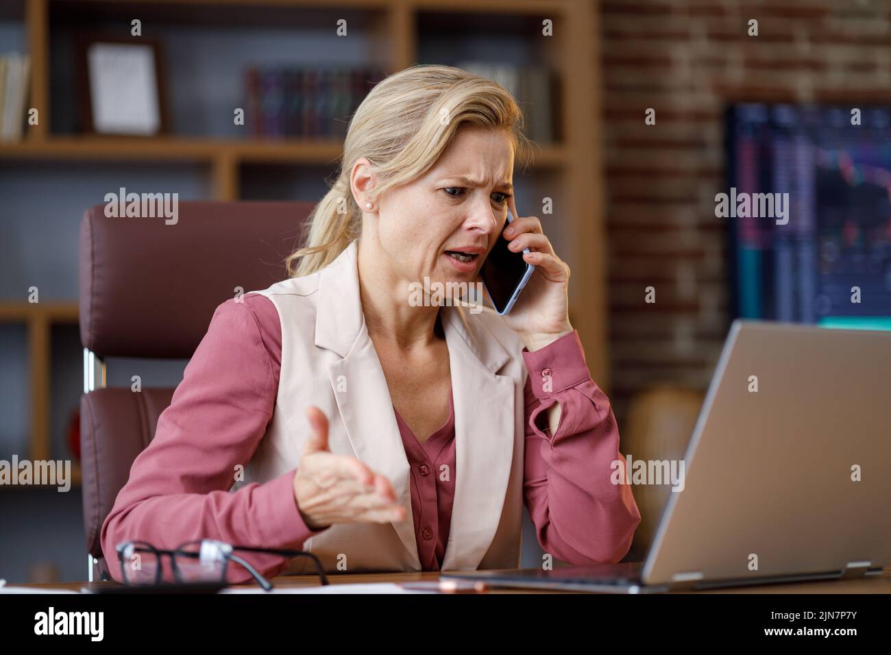 Serious businesswoman having unpleasant phone conversation working on laptop sitting at office. Female trader listening bad news, feels desperate Stock Photo